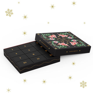 The Cloudberries 12 Days of Christmas Mystery Puzzle is a black, rectangular advent calendar box with gold numbers and a floral lid, surrounded by gold stars and snowflakes—ideal for celebrating the holiday with 1,000 puzzle pieces.