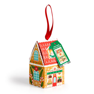 A festive gingerbread house gift box with colorful designs, red ribbon loop, and green tag—perfect for holiday gifting or pairing with Mudpuppy’s Santa's Bakery | 48 Piece Jigsaw Puzzle for extra cheer.