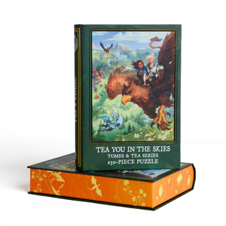 A book-shaped Kingdom of Threads Tea You in the Skies 250 Piece Jigsaw Puzzle box featuring an illustration of two characters riding a large griffin above a village.
