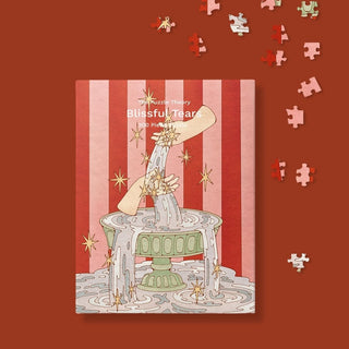 The Puzzle Theory's Blissful Tears is a 300-piece eco-friendly jigsaw puzzle featuring artwork of a hand pouring water into a fountain against a red and pink striped background with scattered puzzle pieces.