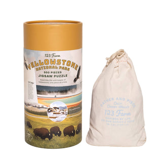 The Yellowstone | 500 Piece Jigsaw Puzzle by 123 Farm comes in a cylindrical box and includes a drawstring bag labeled 123 Farm.