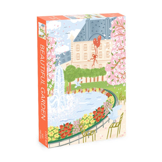 The Beautiful Garden | 500 Piece Jigsaw Puzzle by Olleo Puzzles features a vibrant illustrated garden scene inspired by the Luxembourg Gardens, with trees, flowers, a fountain, and a grand building on the colorful box.