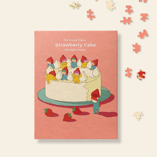The Puzzle Theory’s Strawberry Cake | 300 Piece Jigsaw Puzzle features cartoon gnomes on a cake with strawberries and scattered puzzle pieces.