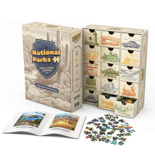 National Parks Puzzle Advent Calendar Vol. 2 box with twelve drawers labeled with national parks, placed beside a guide and a scattered pile of landscape puzzles.