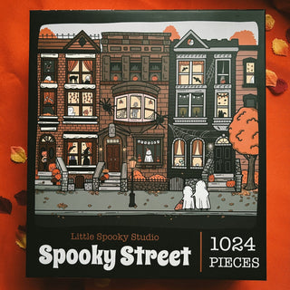 Spooky Street | 1,024 Piece Jigsaw Puzzle by Little Spooky Studio features illustrated houses with Halloween decor, ghosts, and autumn leaves—perfect for cozy fall nights.