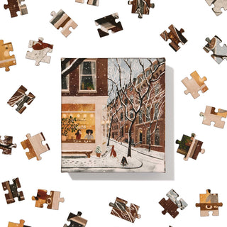 Ordinary Habit's Coffee in the West Village 100 Piece Jigsaw Puzzle features a snowy city street scene with dog walkers, shown completed amid loose pieces on a white background.