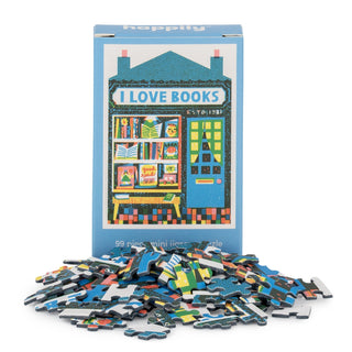A small blue box labeled "Book Shop | 99 Piece Mini Jigsaw Puzzle" by Happily Jigsaw Puzzles features Louise Lockhart's illustrated bookstore facade, surrounded by scattered Book Shop puzzle pieces.