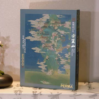 A box of the Yunji Mountain 2,000 Piece Jigsaw Puzzle by PERMA Puzzle, made from Dutch blue-core chipboard and featuring an illustrated landscape, rests on a table beside a small decorative vase.