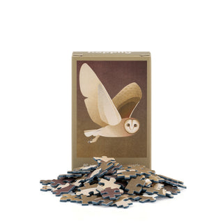 Box featuring an illustration of a flying barn owl, with scattered puzzle pieces in front, set against a white background—Happily Jigsaw Puzzles’ Barn Owl | 99 Piece Mini Jigsaw Puzzle is the perfect wildlife-themed gift for bird lovers.