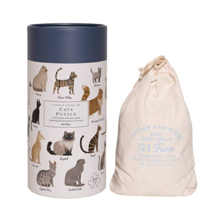 A cylindrical box labeled Cats | 500 Piece Jigsaw Puzzle by 123 Farm, showing cat illustrations and breeds, sits next to a cream drawstring bag with the 123 Farm logo.