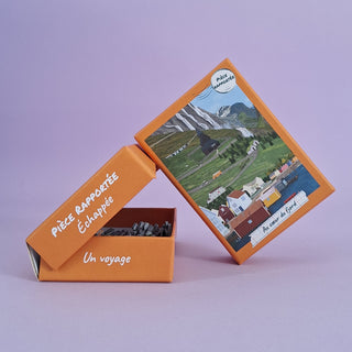 An open orange Pièce Rapportée box reveals the Au Coeur Du Fjord 100-piece jigsaw puzzle. The lid features an illustrated landscape with houses, mountains, and the title "Au Coeur Du Fjord.