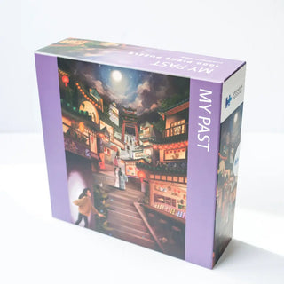 Arcadia Puzzles’ “My Past” is a 1,000-piece jigsaw puzzle in a purple box, depicting a lantern-lit night street scene. Presented in sustainable, matte-finish packaging.