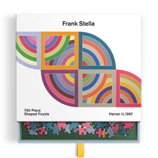 Chronicle Books’ Frank Stella Harran II | 750 Piece Jigsaw Puzzle showcases Stella’s vivid 1967 masterpiece from the Protractor series, with striking geometric patterns and colorful arcs—its box features a partially opened drawer displaying the intricate puzzle pieces inside.