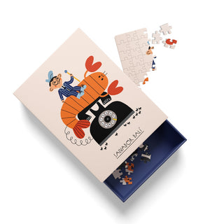 A partially assembled 99-piece jigsaw puzzle rests beside its box, which showcases Ohh Deer’s Salvador Dali design: an illustrated figure riding an orange lobster phone. The box bears the name “Salvador Dali,” reflecting the whimsical surrealism that defines this unique puzzle.