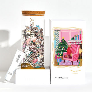 A reusable glass jar of puzzle pieces, glue, and the Jiggy Puzzles "A Whippet Christmas | 800 Piece Jigsaw Puzzle," featuring festive travel art with a whippet by a Christmas tree.