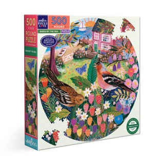 The eeBoo "Birds by the Sea" 500-piece round puzzle features vibrant, whimsical artwork by Lee Foster Wilson with birds, strawberries, flowers, and a house in a lively outdoor scene. Sustainably sourced materials.