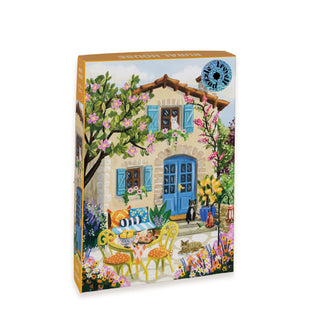 The Trevell Rural House 500 Piece Jigsaw Puzzle showcases a delightful illustration of a stone house with blue shutters and a blue door, complete with a garden table and chairs, blooming flowers, plus a cat and dog in the yard. Made in Turkey, this charming puzzle arrives neatly packaged in a cotton bag for convenient storage.