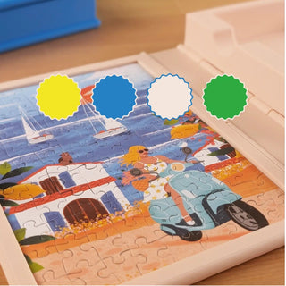 A partially completed mini puzzle from The Puzzle Book by Heol Editions rests in a plastic tray, illustrating a coastal scene with a woman on a scooter, buildings, and boats. Four color swatches are displayed above the puzzle, while a 3D-printed puzzle accessory from Heol Editions adds a unique touch to this playful puzzling experience.