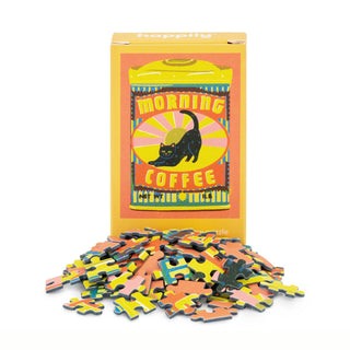 A box of Happily Jigsaw Puzzles' Morning Coffee | 99 Piece Mini Jigsaw Puzzle, featuring a black cat illustration, stands behind vibrant puzzle pieces—evoking the charm of Naomi Wilkinson’s playful coffee-themed designs.