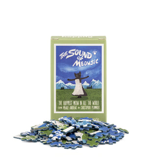A box of the Happily Jigsaw Puzzles The Sound of Meowsic | 99 Piece Mini Jigsaw Puzzle, adorned with a delightful cat illustration by Nia Gould, is surrounded by scattered blue, green, and white mini puzzle pieces.