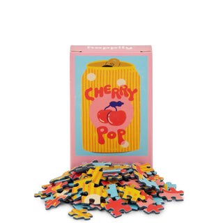 The Cherry Pop | 99 Piece Mini Jigsaw Puzzle by Happily Jigsaw Puzzles showcases an illustrated soda can and cherries on the box, with colorful mini puzzle pieces arranged in front.