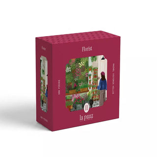 A maroon puzzle box labeled Florist features Rachel V. Hillis’s charming illustration of a woman in a flower shop surrounded by plants. This 280-piece flower shop puzzle is by la pauz.