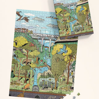 The nearly finished "The Ravine" 1,000-piece jigsaw puzzle by Mango Puzzles shows a lively park with trees, birds, water, and a bridge, with the box and several loose pieces visible nearby.