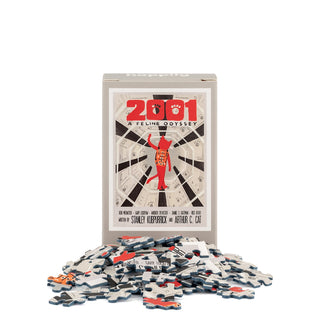 A puzzle box labeled “2001 A Feline Odyssey | 99 Piece Mini Jigsaw Puzzle” by Happily Jigsaw Puzzles stands behind scattered pieces, showcasing a cat-themed parody of the iconic 2001: A Space Odyssey movie poster on the cover. Designed by Nia Gould, this charming mini puzzle is perfect for both cat lovers and film enthusiasts.