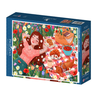 Carpe Diem is a 500-piece jigsaw puzzle by Pieces & Peace, featuring Sandy Ardissone's illustration of a woman on a picnic blanket amid flowers, food, and a basket. Beautifully made in France.