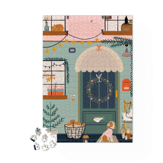The Maison Joliette "Lucky Charm" 500-piece jigsaw puzzle features a festive front door with a wreath, string lights, a dog, and holiday décor; a few pieces remain loose. Perfect for adults, made in France.