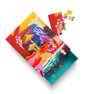 The Ohh Deer “Fungi | 99 Piece Jigsaw Puzzle” showcases a vibrant nature scene illustrated by Natasha Durley, with a partially assembled puzzle and scattered pieces around its partially open box. Dive into the delightful details of this charming, colorful mushroom puzzle as you put it together.