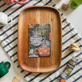 The Sip & Savor | 150 Piece Jigsaw Puzzle by Spaghetti Tree features a teacup image completed on a wooden tray, set amid cups and kitchen items—a delightful, portable scene for puzzle fans.