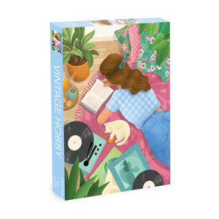 Enjoy the Vintage Hobby | 500 Piece Jigsaw Puzzle by Olleo Puzzles, showcasing a woman reading on a pink rug with her cat, plants, records, and turntable—a cozy scene to piece together.
