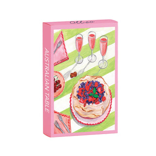 The Australian Table | 99 Piece Jigsaw Puzzle by Olleo Puzzles features a boxed set with pavlova topped with berries, three glasses of pink drink, and utensils on a green and white tablecloth—an authentic Australian scene.
