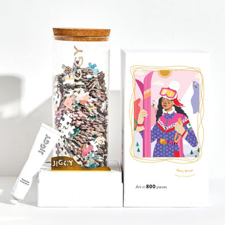 The Retro Winter | 800 Piece Jigsaw Puzzle by Jiggy Puzzles comes in a box with colorful digital illustrations of a skier in pink skis and winter wear, and includes puzzle pieces in a jar plus glue.