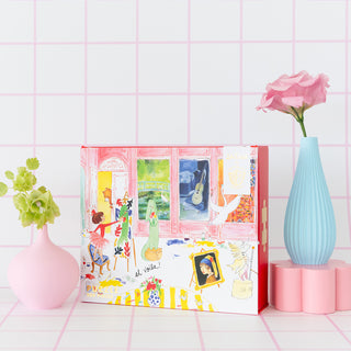 A colorful illustrated box for the Jollity & Co. Lola Dutch | 200 Piece Jigsaw Puzzle sits between a pink vase with green flowers and a blue vase with a pink flower, all set against a white tiled background with pink lines.