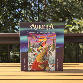 A 1,000-piece “Determination” jigsaw puzzle by Aurora Puzzles, featuring artwork of a King Salmon swimming upstream, with the brand name displayed on the front.