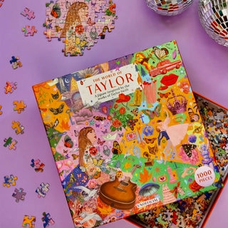 The World of Taylor | 1,000 Piece Jigsaw Puzzle by Laurence King Publishing sits on a purple surface with loose pieces and two disco balls—a perfect Taylor Swift-themed puzzle and gift for any Swiftie.