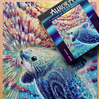 Finished assembling The Selkie, a 500-piece jigsaw puzzle by Aurora Puzzles, featuring a vibrant underwater scene, with its box labeled "Aurora Puzzles" and "The Selkie" displayed on top.