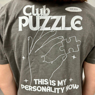 Someone sports the Puzzledly Personality Boxy T-Shirt by Puzzledly, showcasing "Club Puzzle," an outlined hand with a puzzle piece, and the phrase "This is my personality now. EST. 2019.
