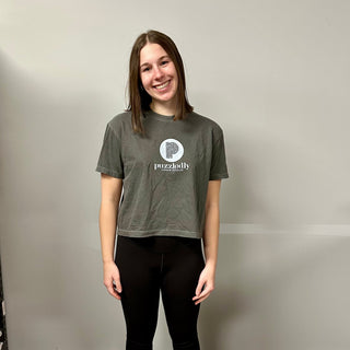 A young woman smiles against a plain wall, wearing the Puzzledly Boxy T-Shirt by Puzzledly and black leggings.