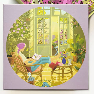 An illustration of a person reading by open French doors in a sunlit, plant-filled room with tea and flowers nearby—just like the tranquil scene in ViSSEVASSE’s Morning Glow 1,000 Piece Jigsaw Puzzle.