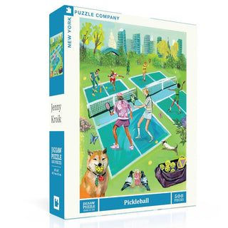 The Pickleball | 500 Piece Jigsaw Puzzle by New York Puzzle Company features an original scene of people playing pickleball on outdoor courts, with a dog, trees, city buildings, and a picnic basket. Includes a linen finish for a premium feel.