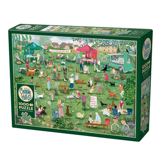 The Cobble Hill “Little Barking Dog Show” 1,000 Piece Jigsaw Puzzle features a charming illustrated outdoor dog show scene with people and dogs, vibrant vendor booths, and a lush, green grassy setting.