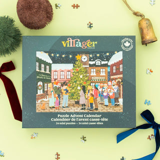 The Villager Puzzles Puzzle Advent Calendar | 24 100 Piece Jigsaw Puzzles by Villager Puzzles features an illustration created by a Canadian woman artist, depicting people gathered around a beautifully decorated Christmas tree in a festive town square, surrounded by cheerful holiday decorations and scattered puzzle pieces. This delightful advent calendar perfectly captures the warmth and joy of the holiday season.