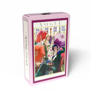 The Penny Puzzle “Spring Parade” is a 99 piece jigsaw puzzle in a rectangular pink box, featuring women with colorful umbrellas on a vintage fashion magazine cover and “Spring Parade” text on the side.