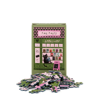 A box labeled Tall Tails from Happily Jigsaw Puzzles features an illustration of a cat and books, surrounded by matching puzzle pieces—this delightful 99 piece mini jigsaw puzzle is part of Nia Gould’s whimsical cat-themed collection.