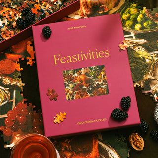 A Feastivities | 1,000 Piece Jigsaw Puzzle by Piecework Puzzles rests on a partially completed jigsaw, surrounded by blackberries and scattered pieces.