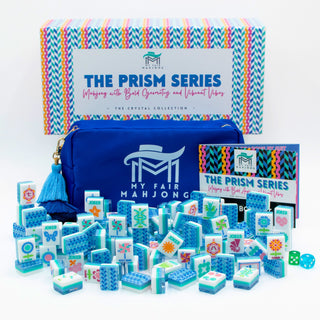 A Crystal Prism Blue | Mahjong Tile Set featuring blue and white tiles with floral patterns, a matching zippered storage bag with a tassel, an instruction booklet, and a patterned storage box.