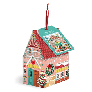 A house-shaped holiday ornament from Galison, styled after a charming Swiss chalet, features a red ribbon handle and a tag with a matching illustration that reads “Swiss Chalet | 130 Piece Jigsaw Puzzle Ornament.”.